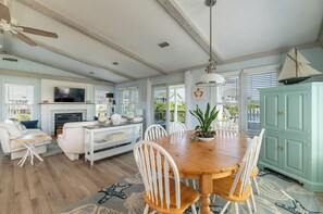 A spacious living room with a fireplace, a dining area with a wooden table and chairs, and a kitchen with light blue cabinets. - Beaulieu-Sur-Duck - Sanderling, Ocean View, Steps to Direct Boardwalk, Pets OK, Flex Stays (Duck)