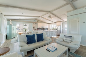 A spacious living room with a white sofa, two armchairs, a coffee table, and a dining area with a wooden table and chairs.