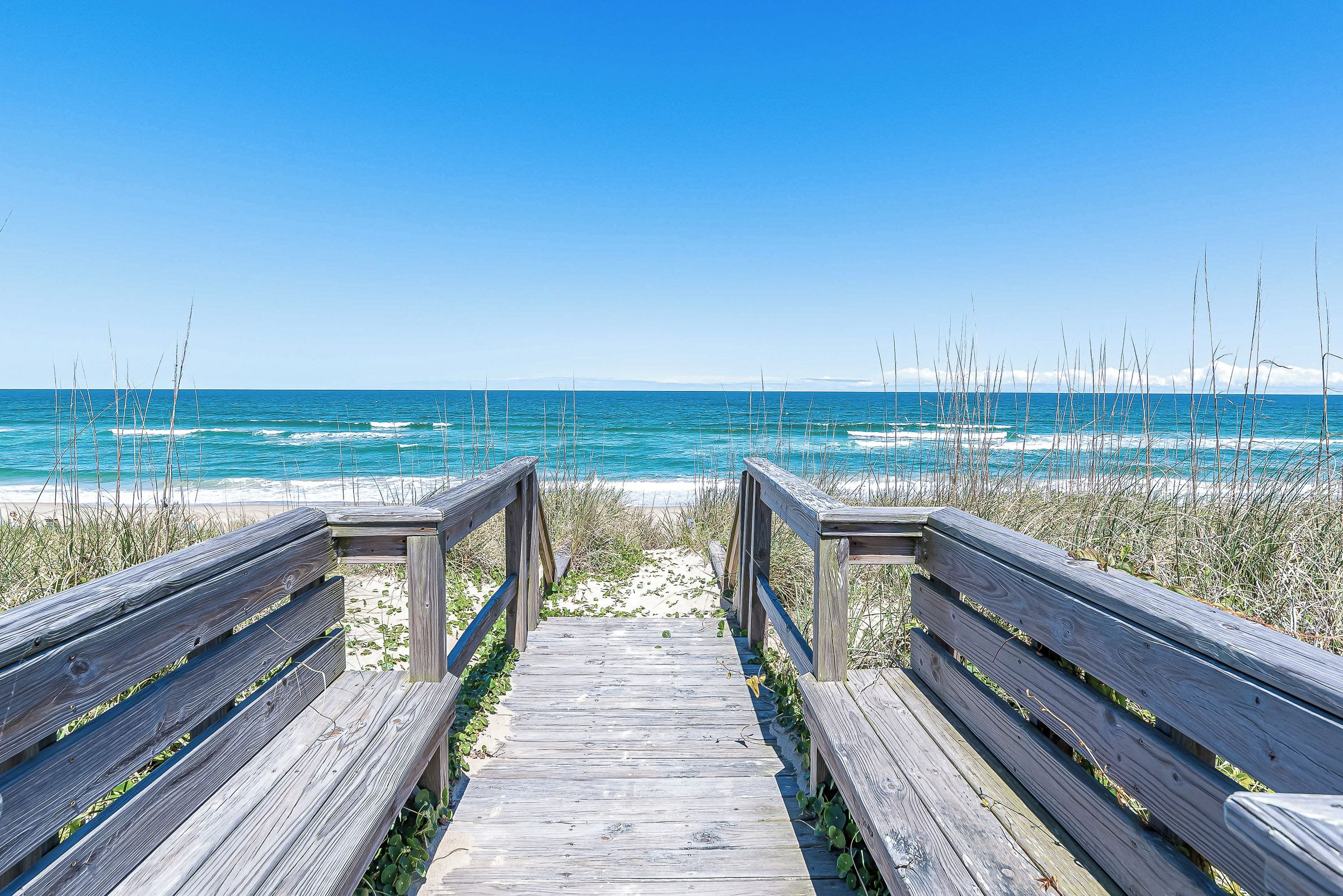 A wooden boardwalk leading to a beach with clear blue water.
