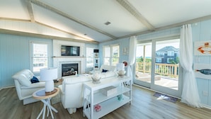 A spacious living room with a fireplace, white furniture, and a large sliding glass door leading to a balcony. - Beaulieu-Sur-Duck - Sanderling, Ocean View, Steps to Direct Boardwalk, Pets OK, Flex Stays (Duck)