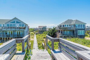 A wooden boardwalk leading to beachfront houses with multiple decks and large windows.