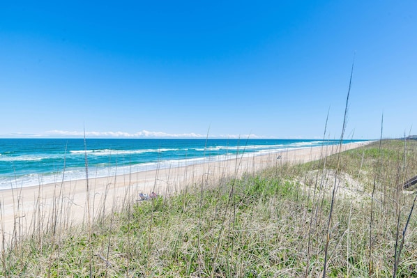 A beach with clear blue water, sandy shore, and grassy dunes. - Beaulieu-Sur-Duck - Sanderling, Ocean View, Steps to Direct Boardwalk, Pets OK, Flex Stays (Duck)