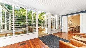 Une pièce spacieuse dotée de grandes portes-fenêtres coulissantes donnant sur un espace extérieur, d’un plancher en bois et d’un coin repas avec des chaises et une table.