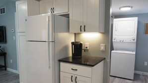 A compact kitchen with white cabinets, a refrigerator, a coffee maker, and a washing machine. - The Red Haven at Conneaut Lake (Conneaut Lake)