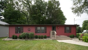 A red single-story house with a front porch, a mailbox, and a small garden area. - The Red Haven at Conneaut Lake (Conneaut Lake)