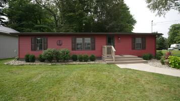 Une maison rouge à un étage, dotée d’un porche à l’avant, d’une boîte aux lettres et d’un petit jardin.