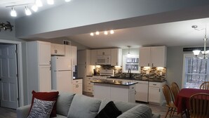 A modern kitchen with white cabinets, a central island, and a dining area with a red tablecloth. - The Red Haven at Conneaut Lake (Conneaut Lake)