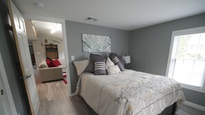 A bedroom with a bed, a nightstand, a window, and a door leading to another room. - The Red Haven at Conneaut Lake (Conneaut Lake)