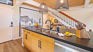 Une cuisine moderne avec des meubles en bois, un plan de travail noir, un évier en acier inoxydable et deux luminaires suspendus.