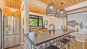 Une cuisine moderne dotée d’un grand îlot central, d’appareils électroménagers en acier inoxydable et de luminaires suspendus.