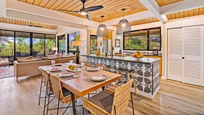 Un vaste espace à manger avec une table et des chaises en bois, une cuisine dotée d’un plan de travail noir et blanc à motifs, et de grandes fenêtres offrant une vue sur l’extérieur.