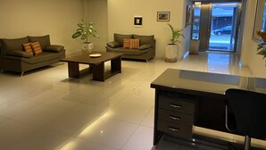 A modern hotel lobby with two sofas, a coffee table, a desk, and a computer. There are potted plants and a framed picture on the wall. - Depto Con Inmejorable Ubicación (Salta)
