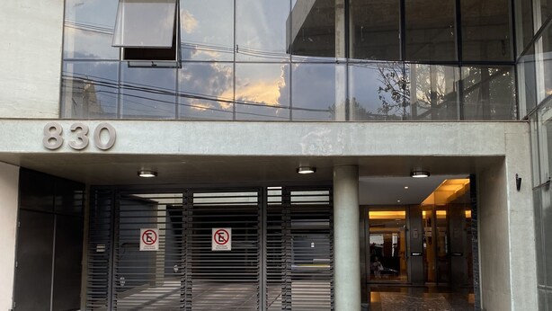 A modern building entrance with a large glass facade, a numbered address sign, and a no parking sign. - Depto Con Inmejorable Ubicación (Salta)