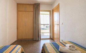 Two single beds with striped bedding, a wardrobe, and a balcony with sliding glass door.