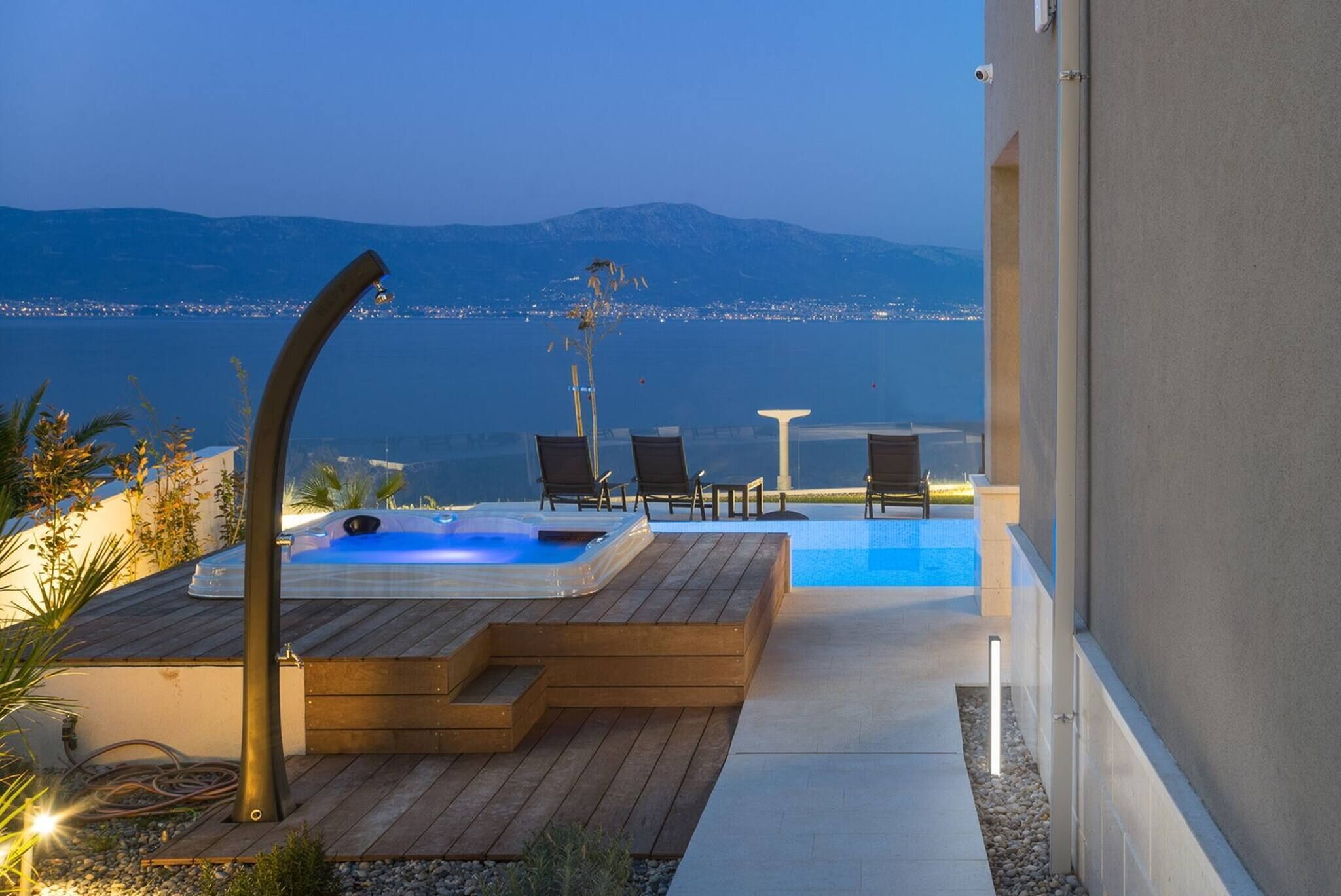 Een hottub met een houten terras, ligstoelen en uitzicht op een stad en bergen.