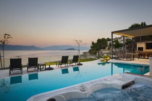 A swimming pool with lounge chairs and a hot tub, overlooking a body of water and mountains. - Luxury Beachfront Villa Paradise Ciovo with Pool (Trogir)