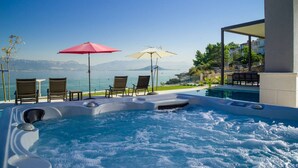 Ein Whirlpool mit Meerblick, zwei Sonnenschirme und Liegestühle.