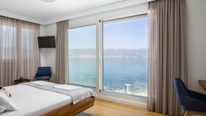 Ein Hotelzimmer mit Bett, Fernseher, Stuhl und einem großen Fenster mit Meerblick.