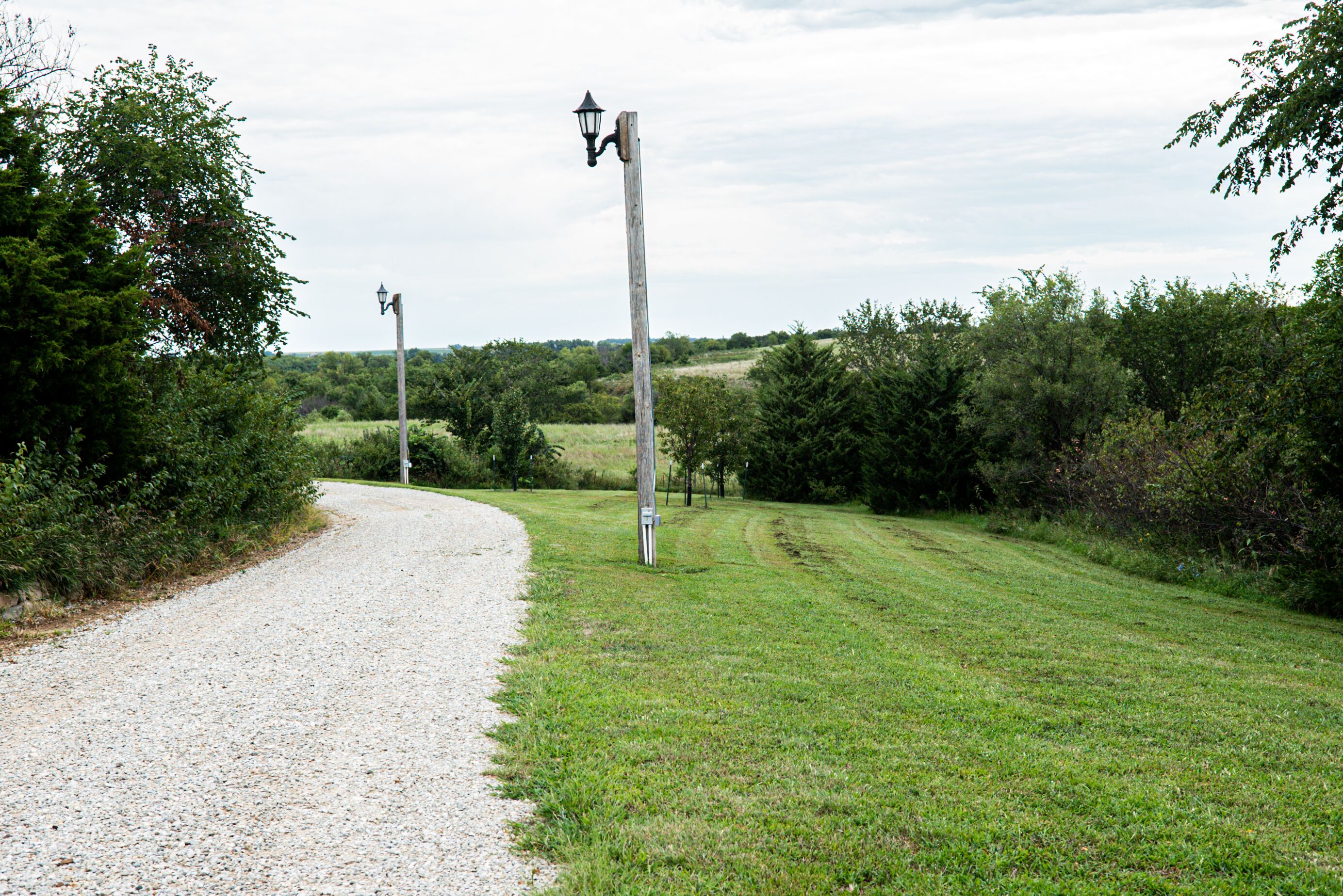 A gravel path leading through a grassy area with two lamp posts.