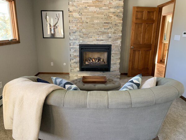 A living room with a stone fireplace, a gray sectional sofa, and a framed deer picture on the wall.