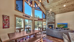 A spacious living room with a stone fireplace, large windows, and a dining area with a wooden table and benches.