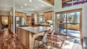 A spacious kitchen with wooden cabinets, a large island with bar stools, and a view of a snowy deck through glass doors.