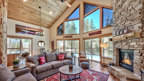 A spacious living room with a stone fireplace, large windows, and a high ceiling.