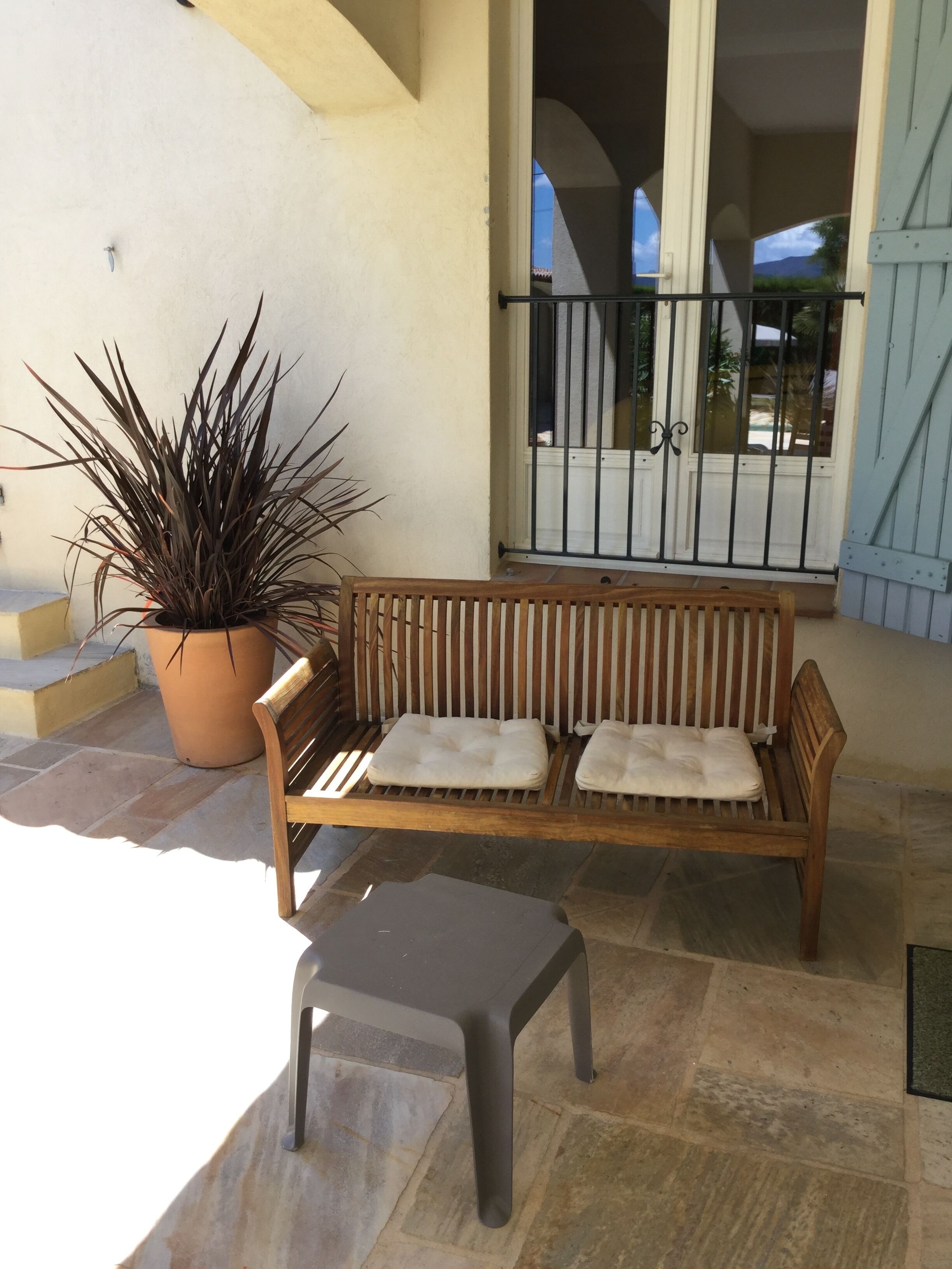 Un banc en bois avec des coussins, une plante en pot et une petite table sur une terrasse carrelée.