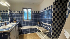 Un baño con baldosas blancas y azules a cuadros, una bañera, un tocador con espejo y una ventana.