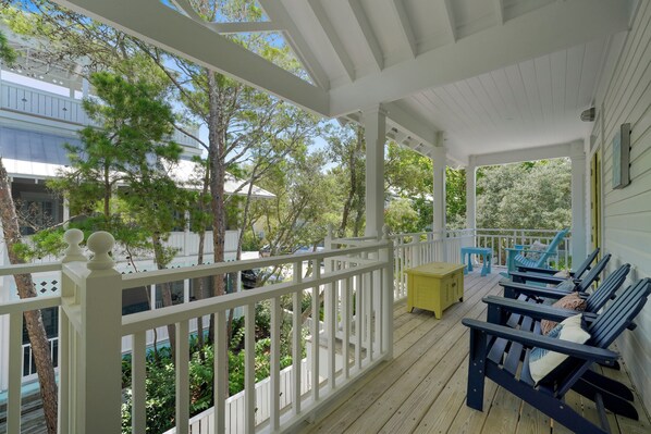 A covered porch with white railings, blue Adirondack chairs, and a yellow table. - Luxury Accommodations in the Heart of Seaside, FL + 2 Adult Bikes! (Santa Rosa Beach)