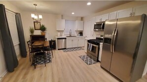 A modern kitchen with white cabinets, stainless steel appliances, and a dining area with a wooden table and chairs.