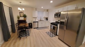 Una cocina moderna con armarios blancos, electrodomésticos de acero inoxidable y un comedor con mesa y sillas de madera.