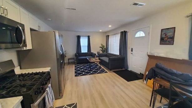 A modern kitchen with a stove, refrigerator, and microwave. There is a dining area with a table and chairs, and a living area with a sofa and a coffee table.
