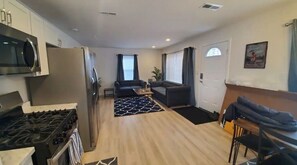 A modern kitchen with a stove, refrigerator, and microwave. There is a dining area with a table and chairs, and a living area with a sofa and a coffee table.