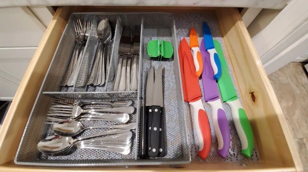 Un tiroir contenant des couverts, des couteaux et des ustensiles de cuisine colorés, tous rangés avec soin.