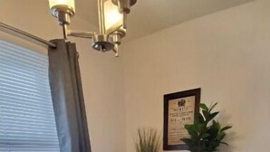 A dining area with a wooden table, black chairs, a black trash bin, a potted plant, and a framed certificate on the wall.