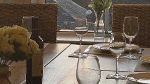 A dining table with four wine glasses and a vase of flowers, set against a backdrop of a sunset over the sea. - Sea views just yards from restaurants, pubs & shops. Sleeps 16-18, 8 x en-suite. (Tintagel)