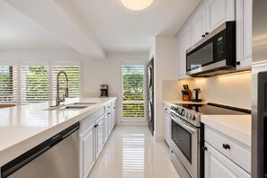 Una cocina moderna con armarios blancos, estufa de acero inoxidable y microondas empotrado.