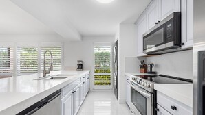Una cocina moderna con armarios blancos, un refrigerador de acero inoxidable, horno empotrado y microondas.