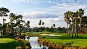 Un campo de golf con un estanque, palmeras y cielo despejado.