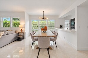 A modern kitchen with a dining area, featuring a wooden table, chairs, and a central light fixture.