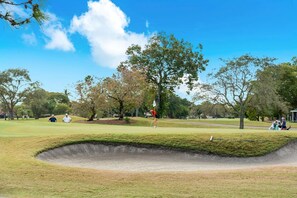 Un parcours de golf avec un bunker de sable, des arbres et des personnes qui jouent.