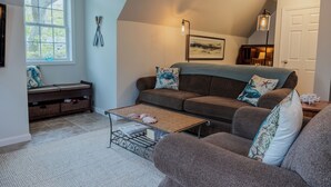 A cozy living room with a brown sofa, a glass coffee table, and a bench with storage baskets. - Immaculate Coastal Retreat! (Tisbury)