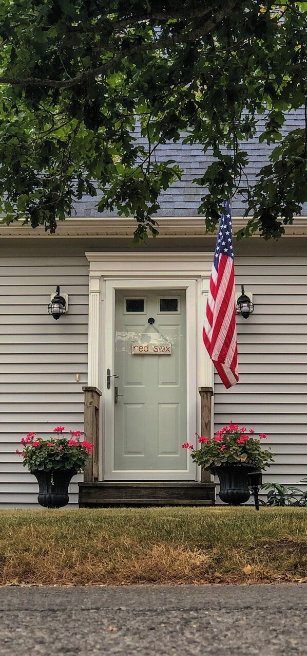 A house with a white door, an American flag, and two flower pots. - Immaculate Coastal Retreat! (Tisbury)