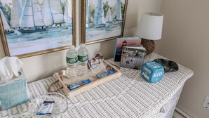 A hotel room with a wicker table, a lamp, a tray with toiletries, and two framed paintings of sailboats. - Immaculate Coastal Retreat! (Tisbury)