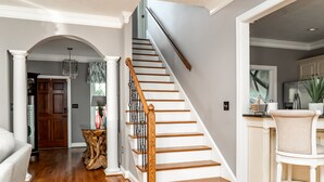 Eine Treppe mit Holzboden und Geländer führt zu einer Zwischenebene mit einer weißen Tür und einem Holztisch mit einer Vase.