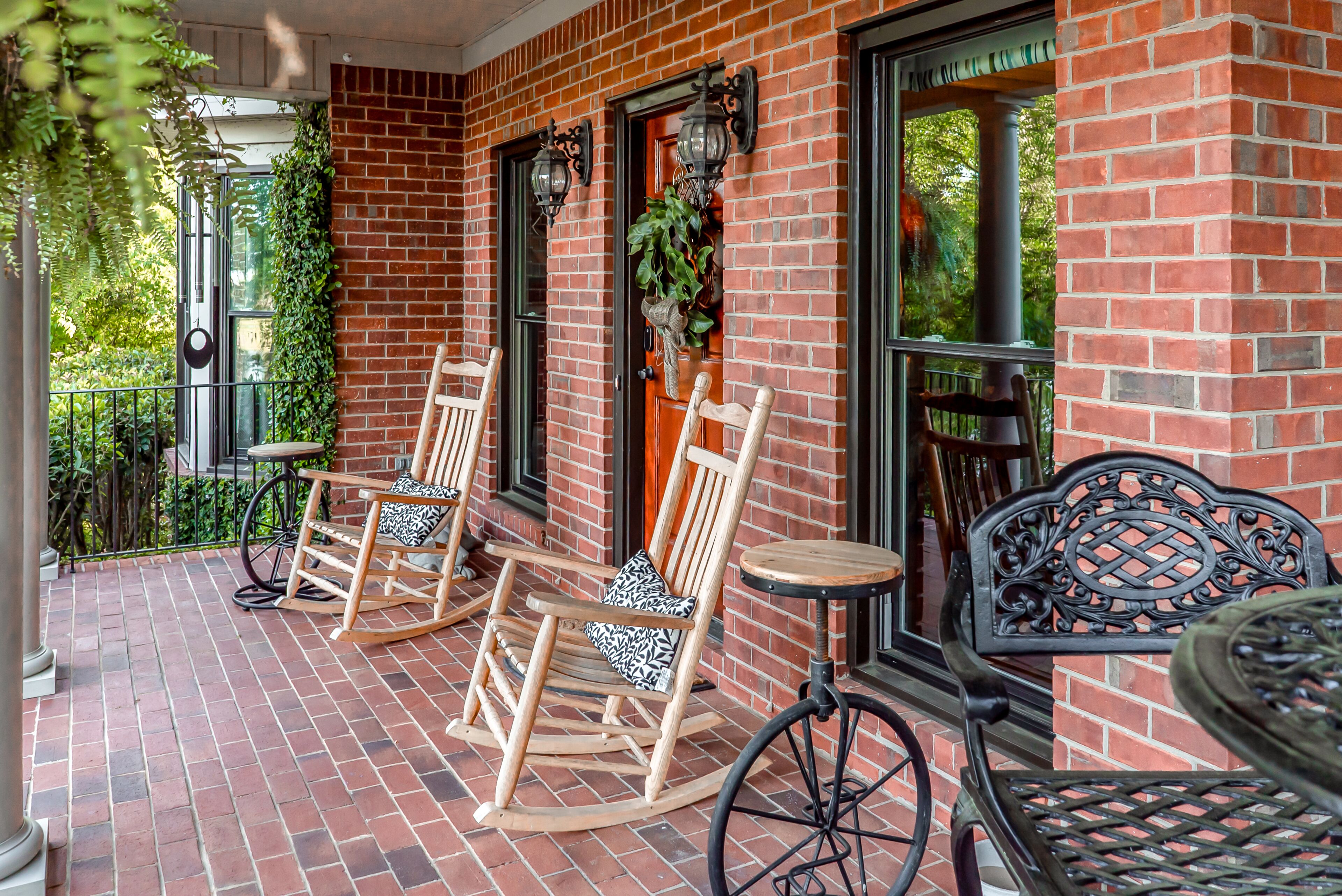 Een gebouw van baksteen met een veranda, voorzien van schommelstoelen en een kleine tafel.