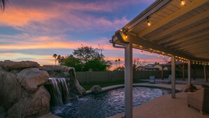 A swimming pool with a waterfall feature, surrounded by rocks and a covered patio area with lounge chairs. - Relaxing 4 Bdrm Retreat in the Heart of Scottsdale!  Big yard and Heated Pool!  (Scottsdale)