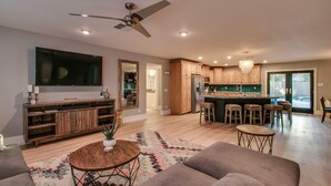 A spacious living room with a large TV, wooden cabinets, a kitchen area with a bar, and a ceiling fan. - Relaxing 4 Bdrm Retreat in the Heart of Scottsdale!  Big yard and Heated Pool!  (Scottsdale)