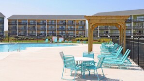 A poolside area with a pool, lounge chairs, and a building with balconies in the background. - Ocean Vue - 1BR Surf Condo - Swimming Pool & Ocean Views! (Surf City)